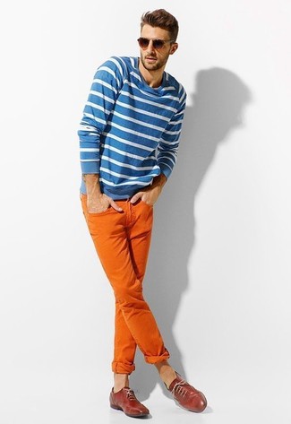 Бело-синий свитер с круглым вырезом в горизонтальную полоску и оранжевые брюки чинос — выгодные инвестиции в твой гардероб. Выбирая обувь, сделай ставку на классику и надень красные туфли.