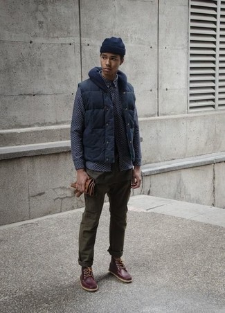 Темно-синяя куртка без рукавов и оливковые брюки чинос — великолепный вариант простого, но стильного лука. Любители экспериментировать могут завершить образ темно-коричневыми рабочими ботинками.