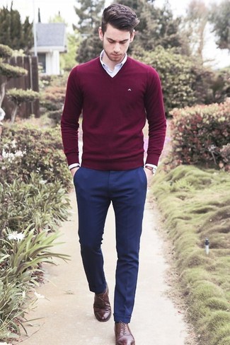 Сочетание темно-красного свитера с v-образным вырезом и темно-синих классических брюк — отличный пример делового городского стиля. Очень выигрышно здесь будут смотреться темно-коричневые кожаные туфли.