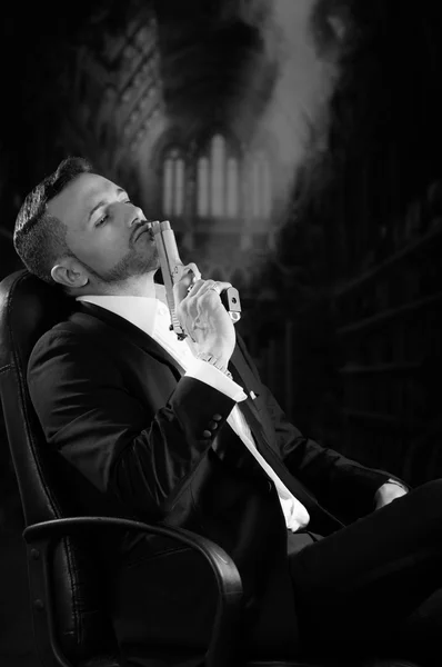 Элегантный мужчина, сидя в кресле, держа пистолет на темном фоне — стоковое фото