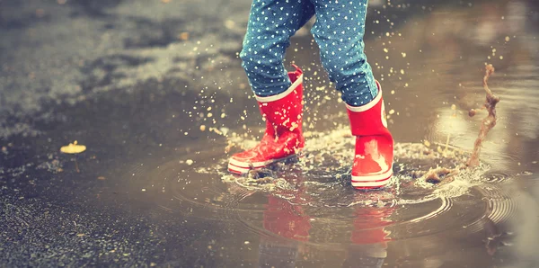 Ножки ребенка в красные резиновые сапоги, прыжки в осенние лужицы — стоковое фото