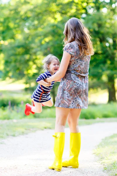 Мать и маленькая восхитительная детская девочка в весело проводящих время резиновых сапогах — стоковое фото