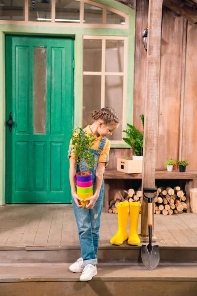 Очаровательны маленькая девочка, холдинг красочные цветочные горшки с дома завод и глядя вниз — стоковое фото